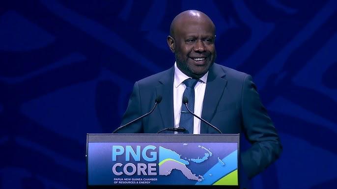 Speaker at a PNGCORE lectern against a blue conference backdrop.