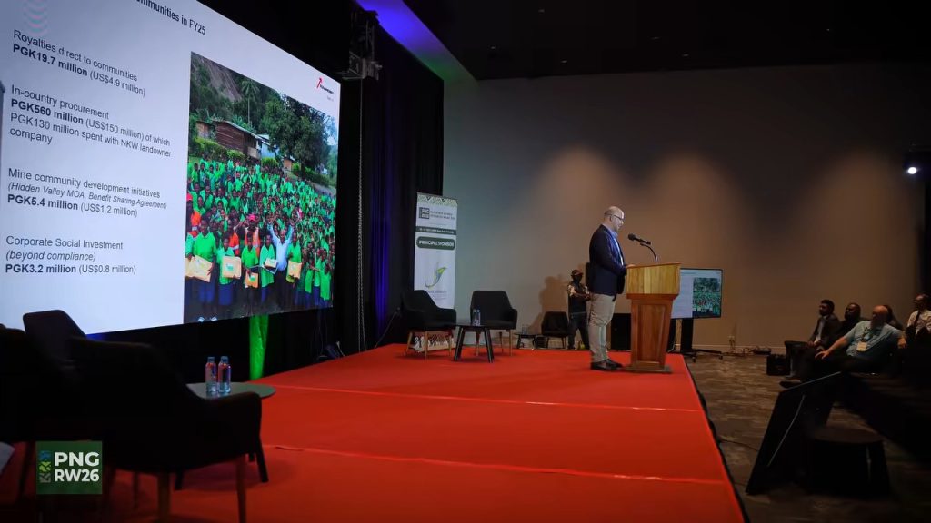 A presenter addresses delegates beside a community benefits presentation at PNG Resources Week 2026